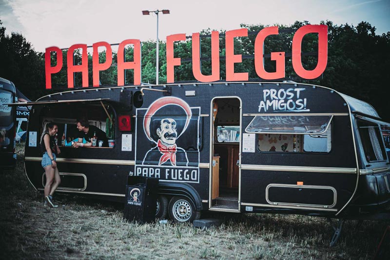 Der stylische Verkaufswagen von Papa Fuego ist geöffnet. Der Verkäufer spricht mit einer Gästin
